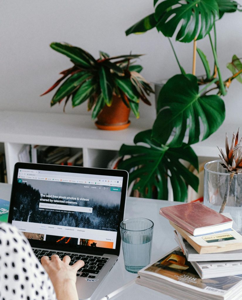 A woman working from home on her laptop surrounded by plants and books for a cozy office feel.